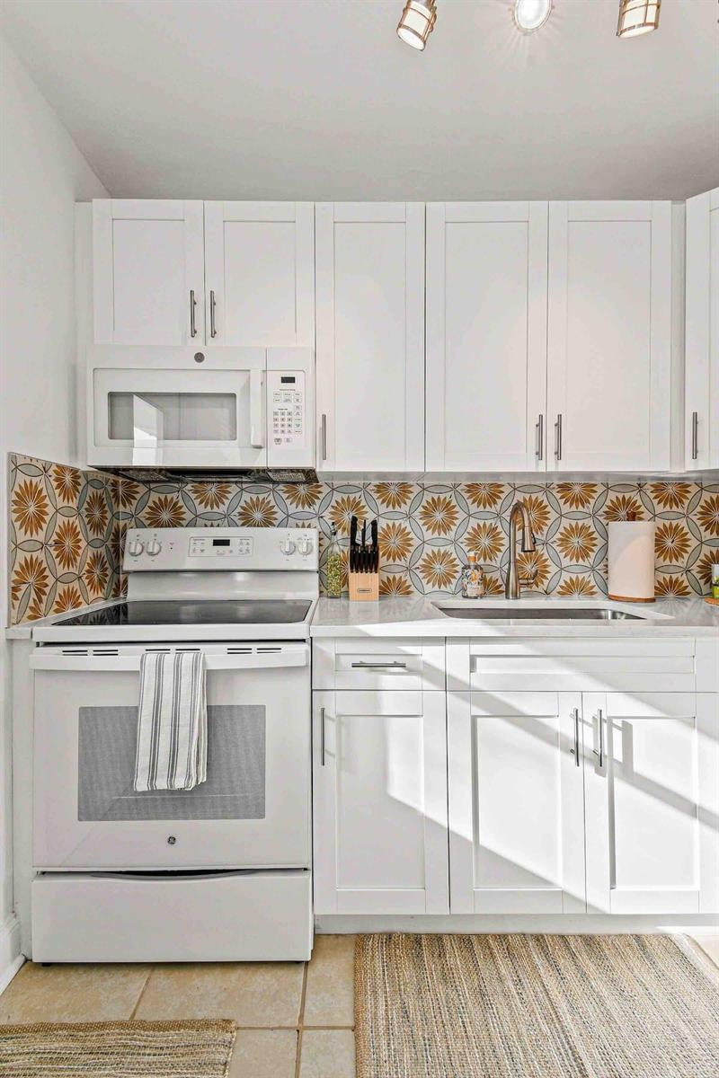 A kitchen features white cabinets, a white stove, and a patterned tile backsplash — 427 Conniston Road # B, West Palm Beach FL 33405, WEST PALM BEACH, FL