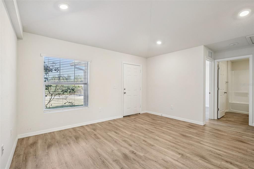 An empty room features light wood-look flooring, white walls, a window, and a white door — 15537 BUICK AVENUE, PORT CHARLOTTE, FL