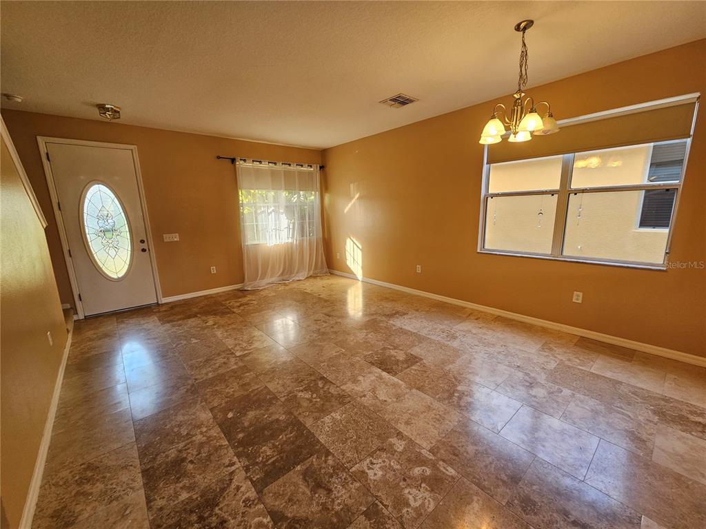 A living room features tan walls, large stone floor tiles, a chandelier, and a front door — 1881 STRATHMORE CIRCLE, MOUNT DORA, FL