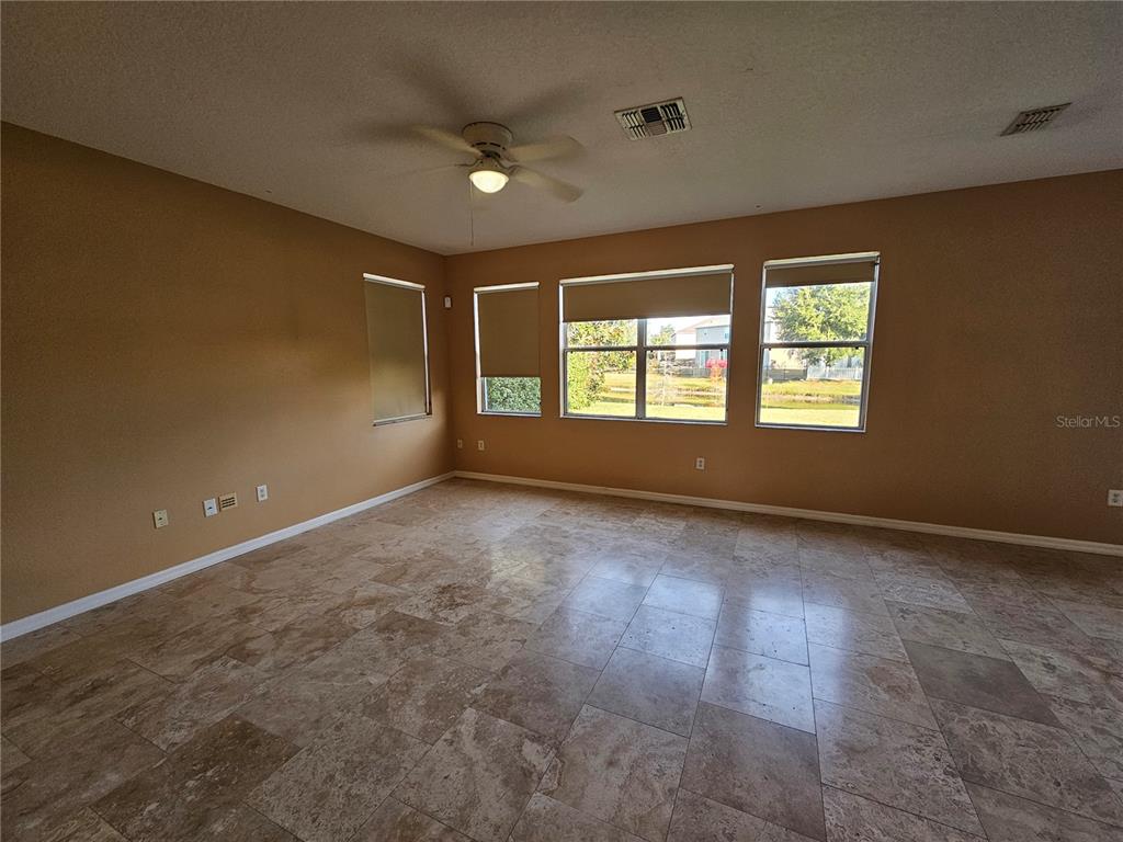 A spacious living room features tan walls, tile flooring, a ceiling fan, and large windows — 1881 STRATHMORE CIRCLE, MOUNT DORA, FL