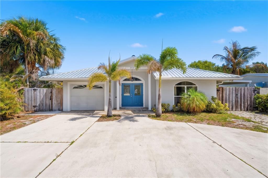 A single-story house with a metal roof, blue double doors, and palm trees in front — VERO BEACH, FL