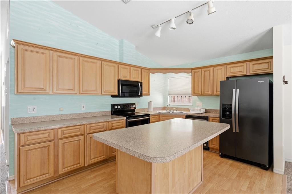 A kitchen features light wood cabinets, laminate countertops, black appliances, and a central island — VERO BEACH, FL