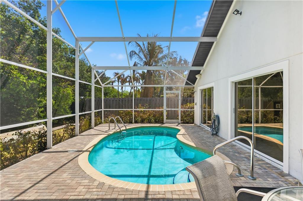 A screened-in patio features a kidney-shaped swimming pool surrounded by brick pavers — VERO BEACH, FL