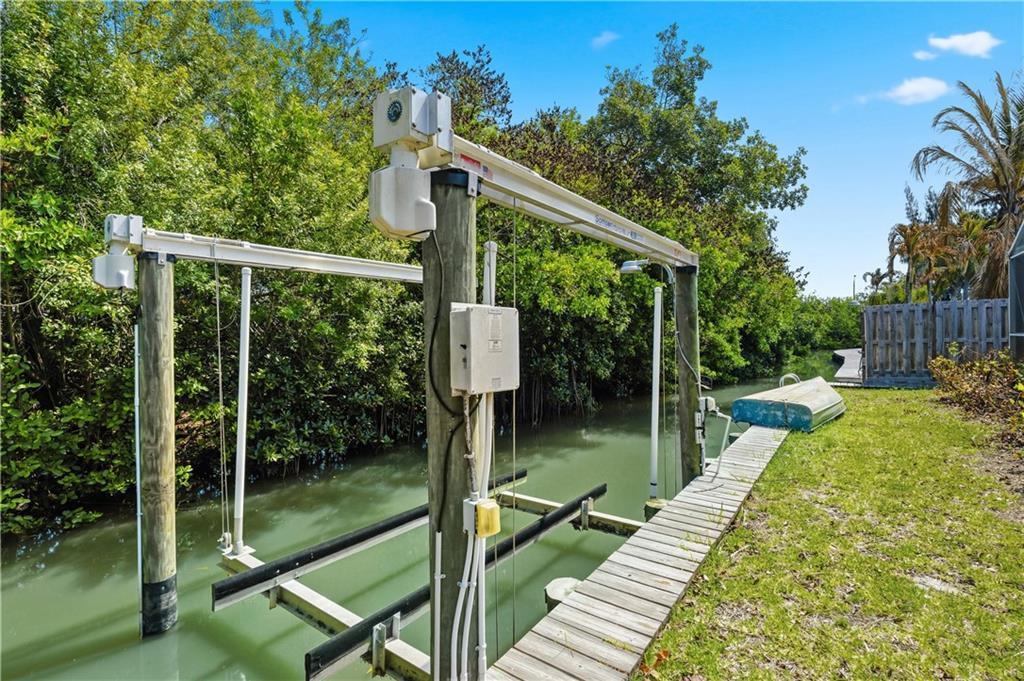 A boat lift with wooden pilings and metal tracks sits over a canal near mangroves — VERO BEACH, FL