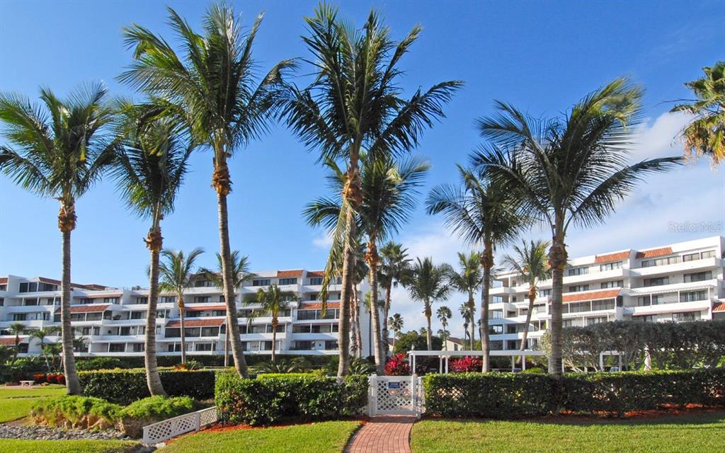 A white multi-story apartment building stands behind a row of palm trees and a hedge — 1485 GULF OF MEXICO DRIVE UNIT 109, LONGBOAT KEY, FL
