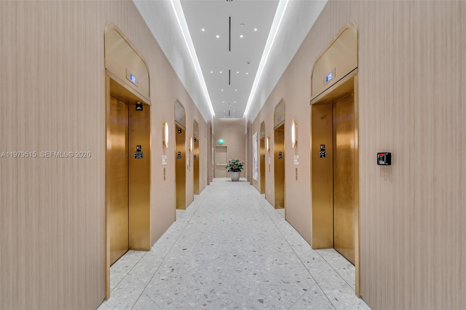 A hallway features light wood-paneled walls, gold elevator doors, and a speckled stone floor — 77 SE 5TH ST # 2405, Miami FL 33131, MIAMI, FL
