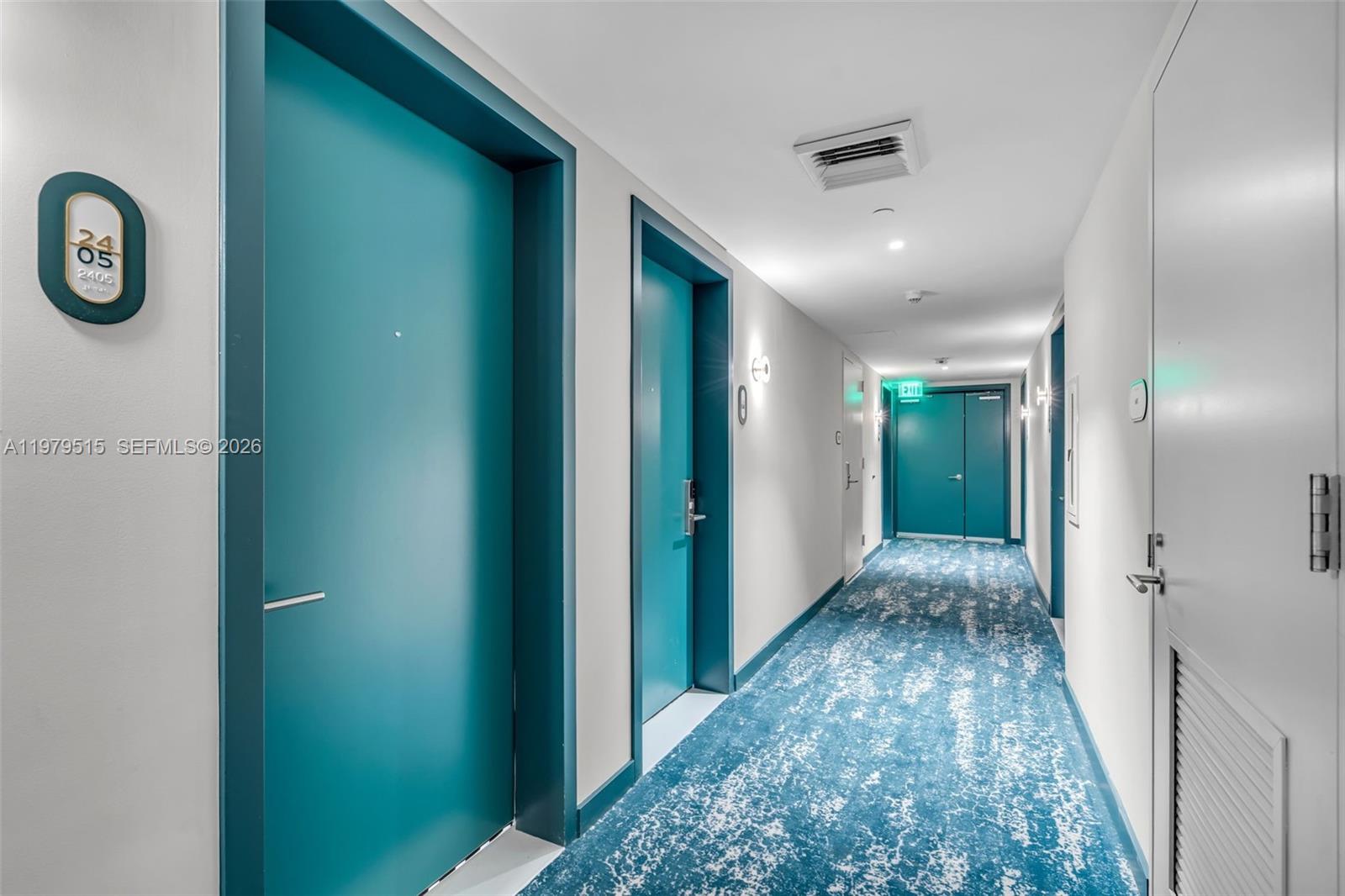 A hallway features teal doors, patterned blue carpeting, and white walls with recessed lighting — 77 SE 5TH ST # 2405, Miami FL 33131, MIAMI, FL