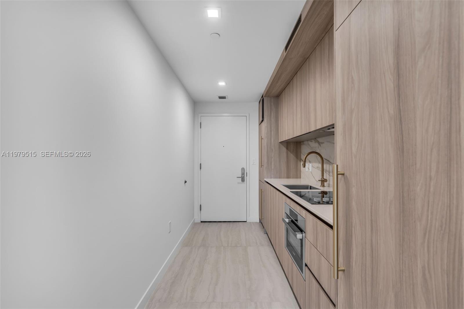 A narrow kitchen features light wood cabinetry, a white door, and neutral tile flooring — 77 SE 5TH ST # 2405, Miami FL 33131, MIAMI, FL
