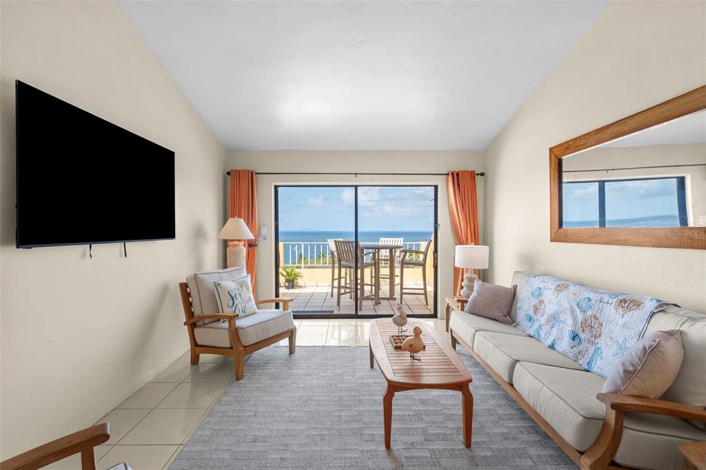 A living room features a sofa, armchair, coffee table, wall-mounted television, and a balcony with ocean views — 295 Palmas Inn Way PALMAS INN WAY UNIT 406, HUMACAO, PR