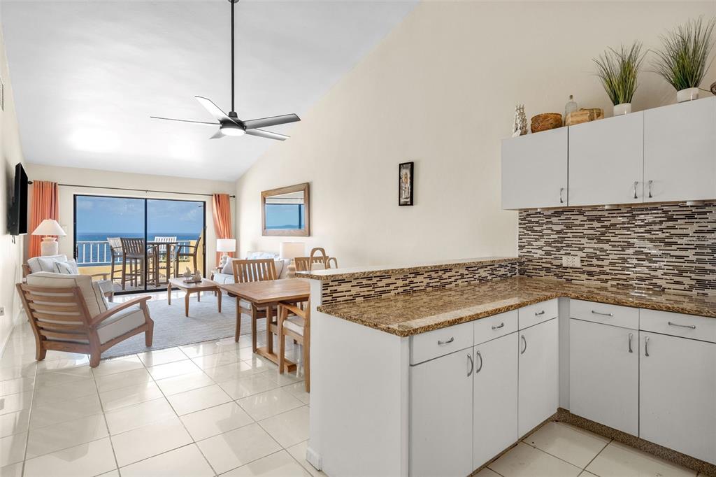 A kitchen with granite countertops and white cabinets overlooks a living area with ocean views — 295 Palmas Inn Way PALMAS INN WAY UNIT 406, HUMACAO, PR