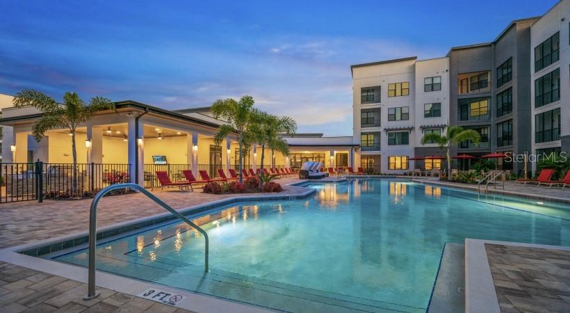A swimming pool with a metal handrail sits in front of a modern apartment building — 8925 77TH TERRACE E UNIT B6-D, LAKEWOOD RANCH, FL