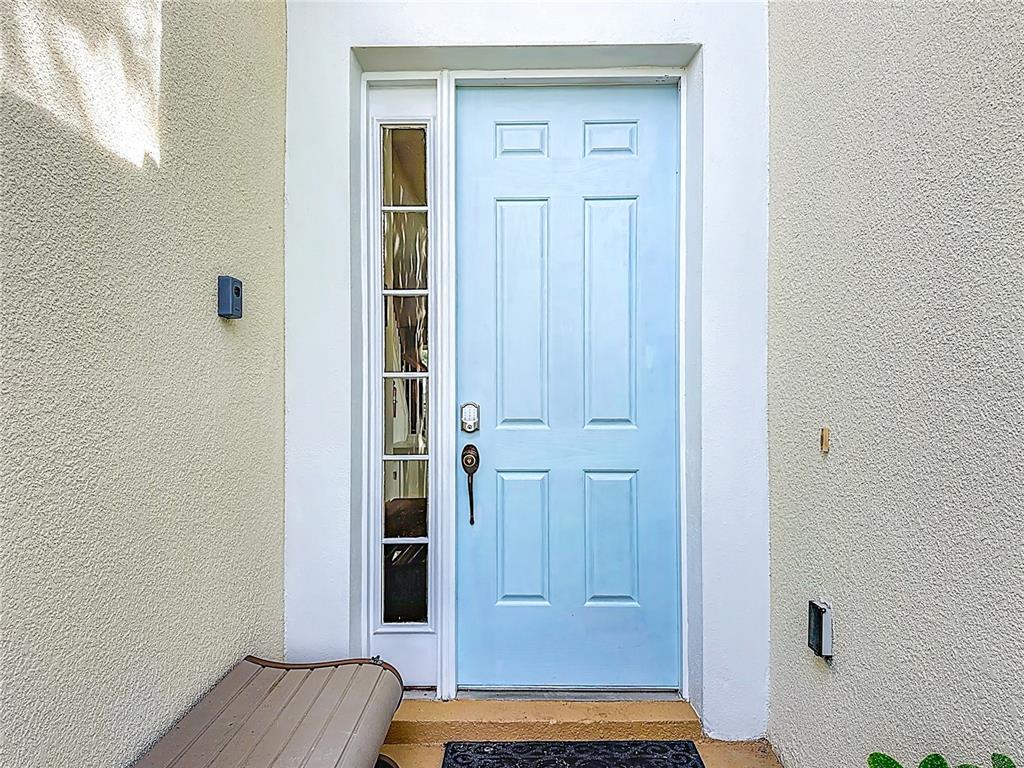 A light blue front door with a side window panel sits between beige stucco walls — 7788 BASNETT CIRCLE, KISSIMMEE, FL
