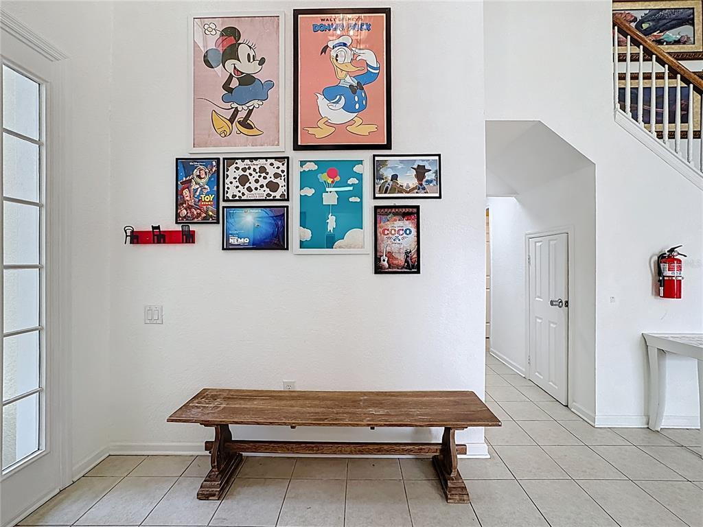 A foyer features a wooden bench, tiled floors, and a gallery wall of Disney-themed posters — 7788 BASNETT CIRCLE, KISSIMMEE, FL