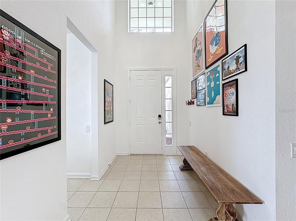 A bright entryway features tiled floors, a wooden bench, and walls decorated with framed posters — 7788 BASNETT CIRCLE, KISSIMMEE, FL