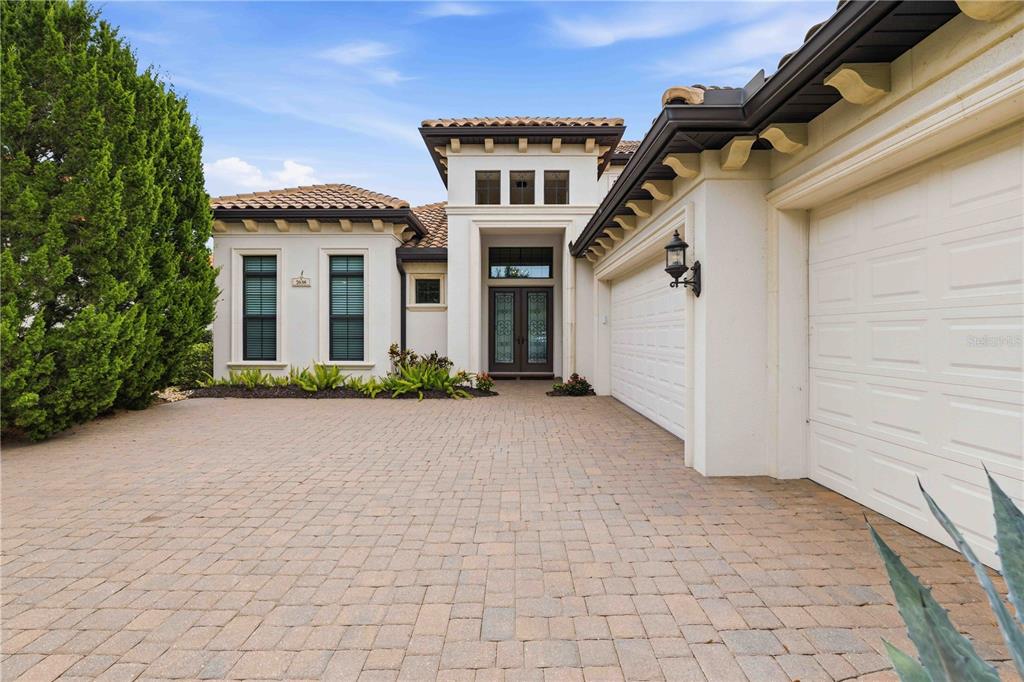 A Mediterranean-style house exterior with a paved driveway, a two-car garage, and a recessed entryway — 7638 WINDY HILL COVE, BRADENTON, FL
