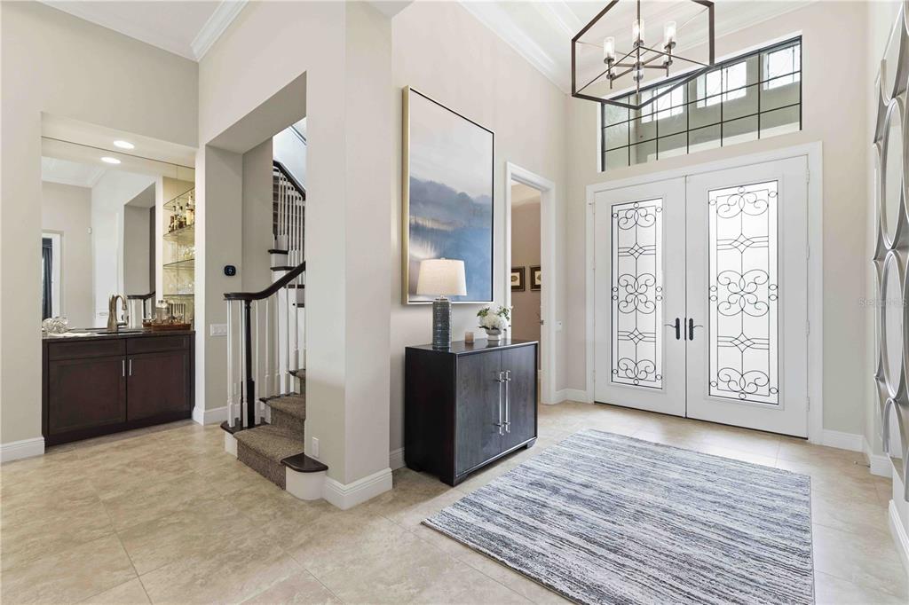 A bright foyer features a double-door entrance, a dark wood console table, and a staircase — 7638 WINDY HILL COVE, BRADENTON, FL