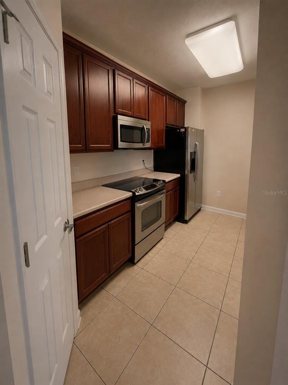 A kitchen features dark wood cabinets, stainless steel appliances, and beige tile flooring — 3338 ROBERT TRENT JONES DR UNIT 203, ORLANDO, FL