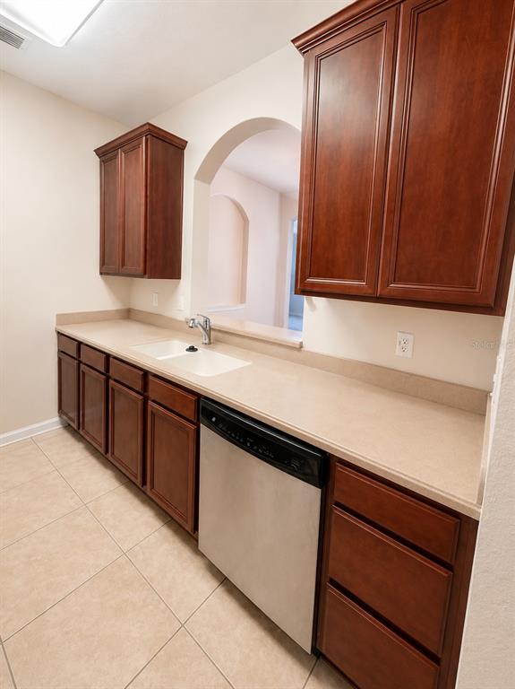 A kitchen features dark wood cabinets, beige countertops, a white sink, and a stainless dishwasher — 3338 ROBERT TRENT JONES DR UNIT 203, ORLANDO, FL