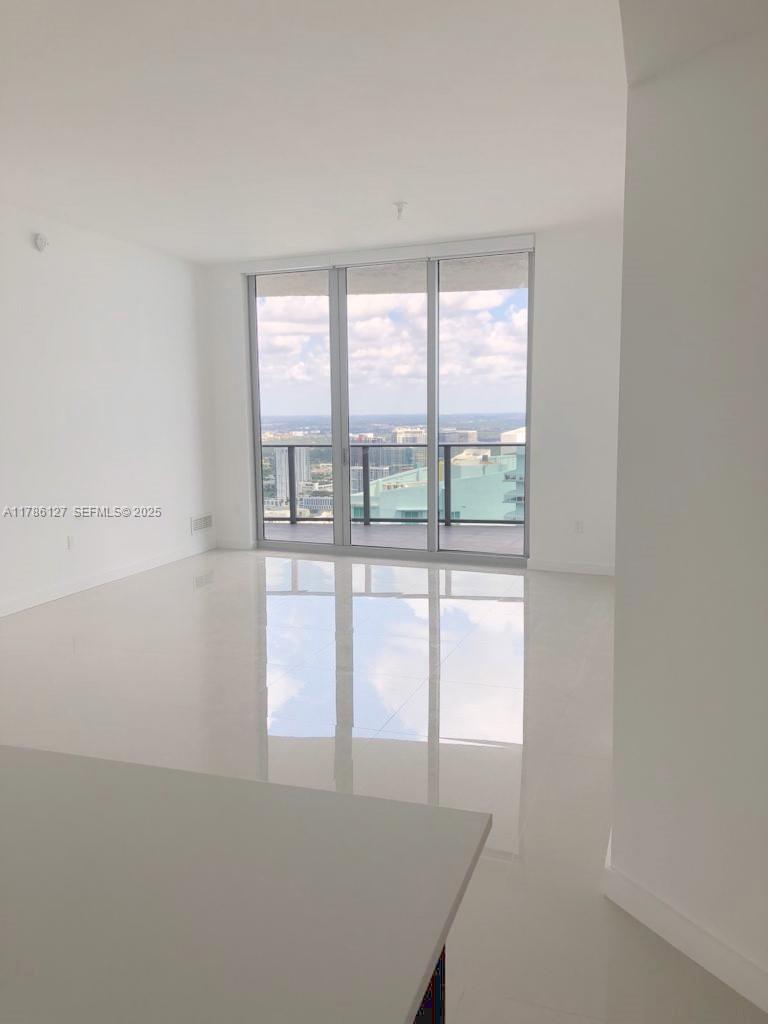 A bright, minimalist room features white tile floors, white walls, and floor-to-ceiling glass balcony doors — 488 NE 18th St # 4905, Miami FL 33132, MIAMI, FL