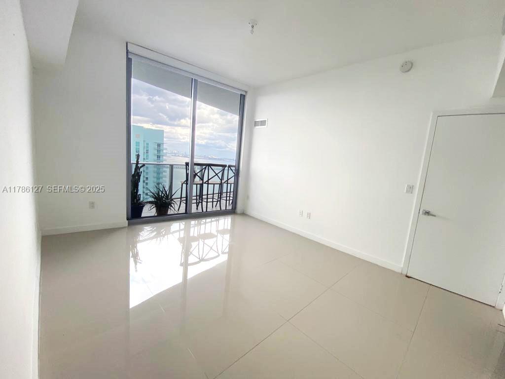 An empty room features white walls, light tile flooring, and a sliding glass door to a balcony — 488 NE 18th St # 4905, Miami FL 33132, MIAMI, FL
