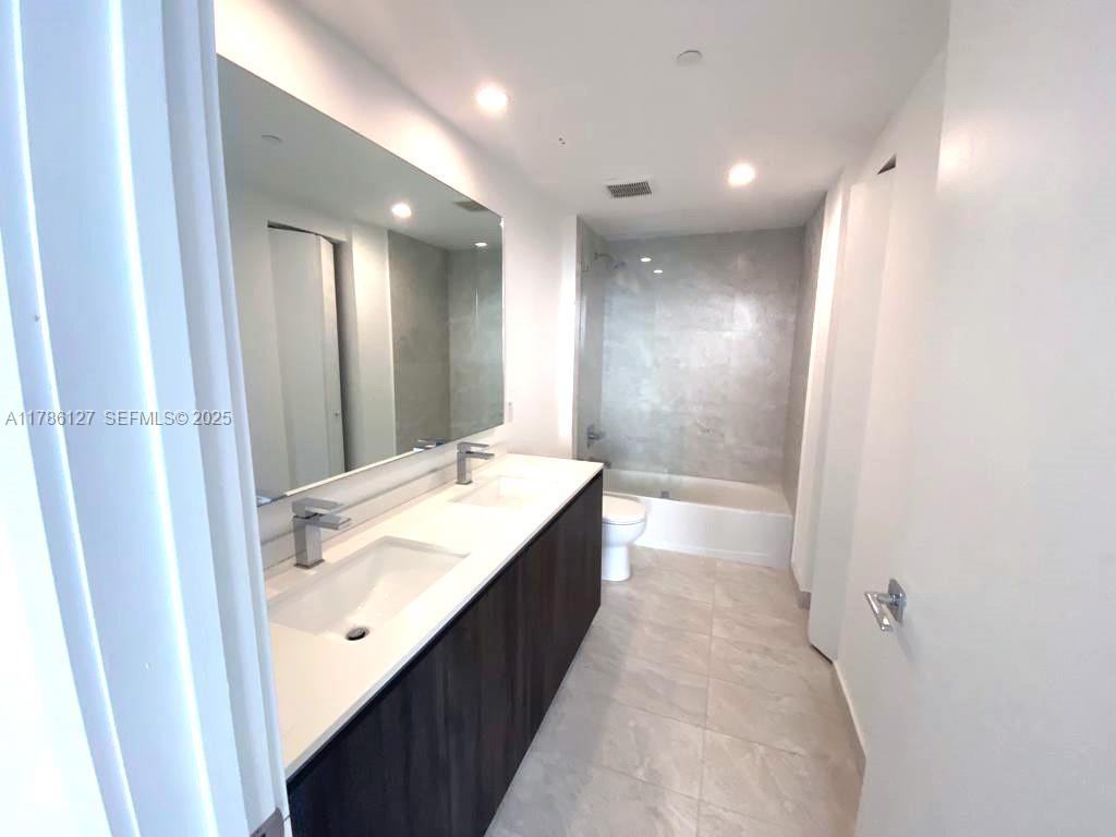 A modern bathroom features a double vanity with a large mirror and a tiled tub — 488 NE 18th St # 4905, Miami FL 33132, MIAMI, FL