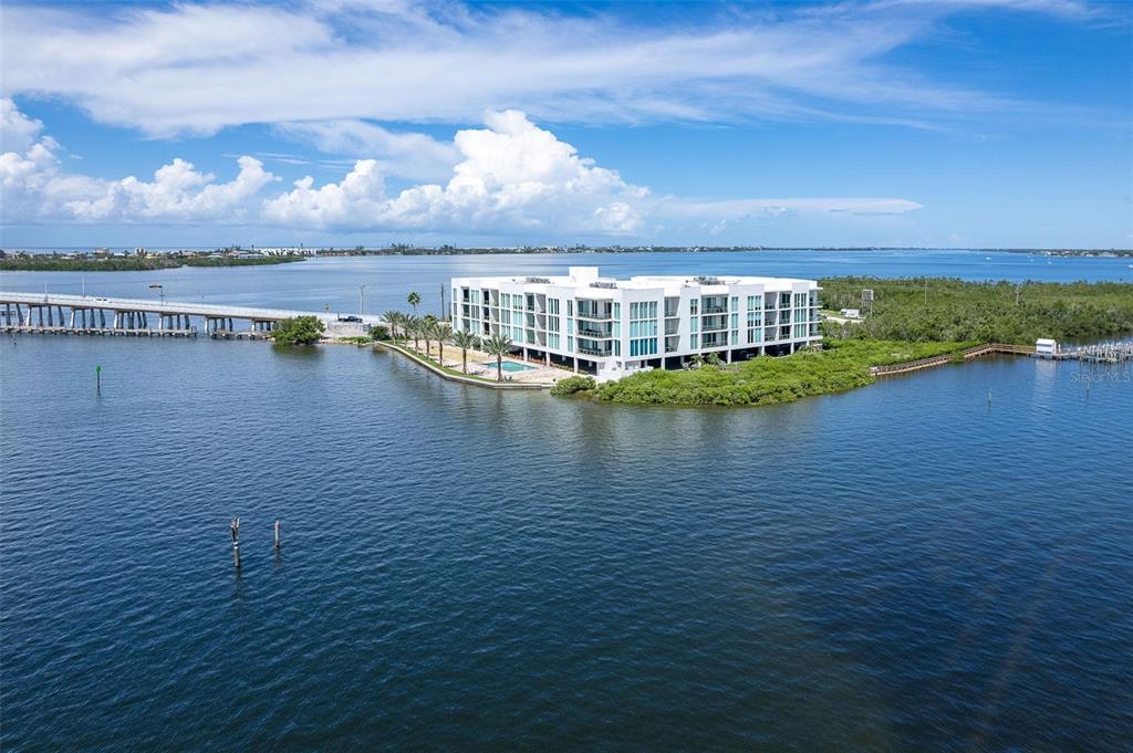 An aerial view shows a multi-story white waterfront condominium building with a pool and bridge — 1375 BEACH ROAD UNIT 309, ENGLEWOOD, FL