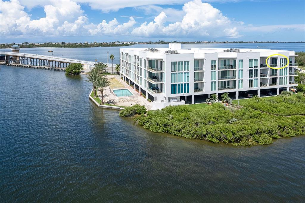 An aerial view shows a modern white apartment building situated on a peninsula near a bridge — 1375 BEACH ROAD UNIT 309, ENGLEWOOD, FL