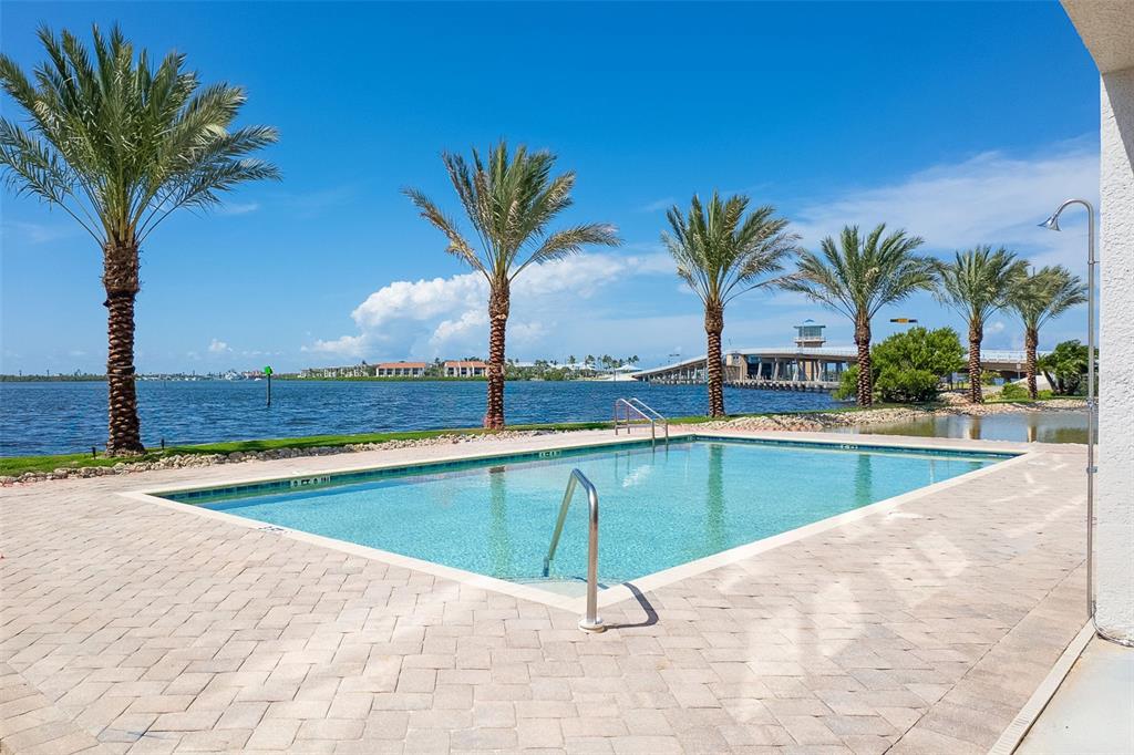 A rectangular swimming pool sits on a paved patio overlooking a bay with palm trees — 1375 BEACH ROAD UNIT 309, ENGLEWOOD, FL