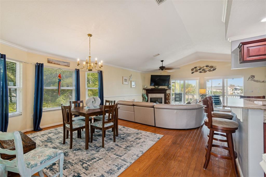 An open-concept living and dining area features hardwood floors, a vaulted ceiling, and a fireplace — 6170 SEASIDE DRIVE, NEW PORT RICHEY, FL