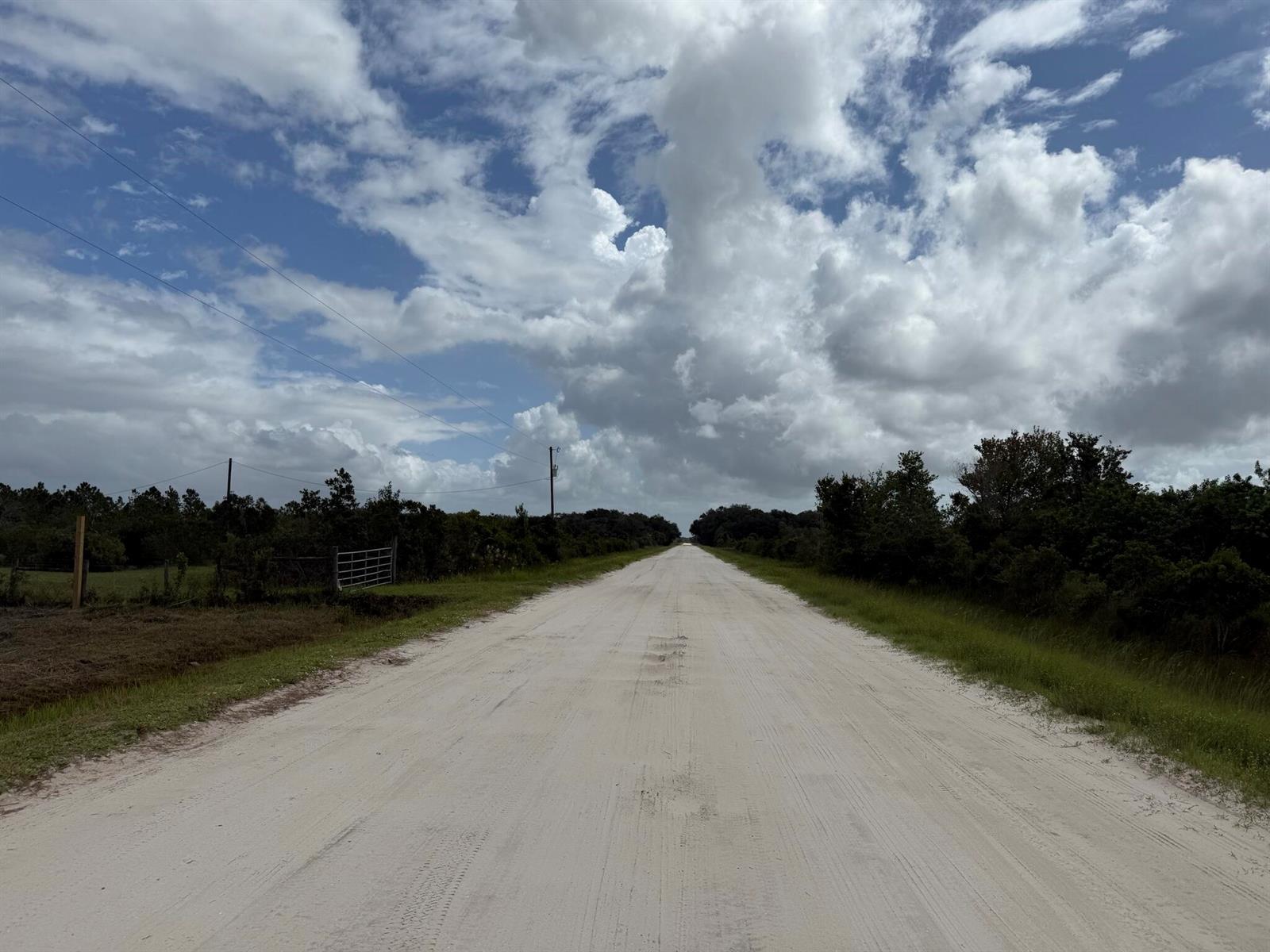 A long, straight dirt road stretches toward the horizon under a cloudy blue sky — 15723 NW 304th Street, Okeechobee FL 34972, OKEECHOBEE, FL