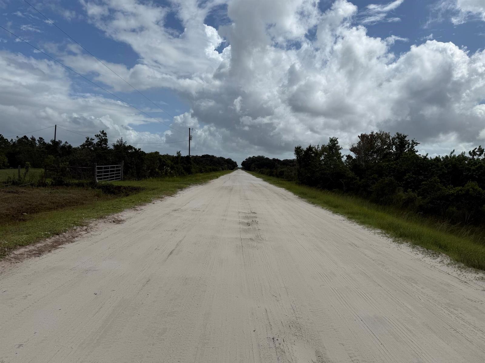A long, straight dirt road stretches through a rural landscape under a cloudy sky — 15723 NW 304th Street, Okeechobee FL 34972, OKEECHOBEE, FL