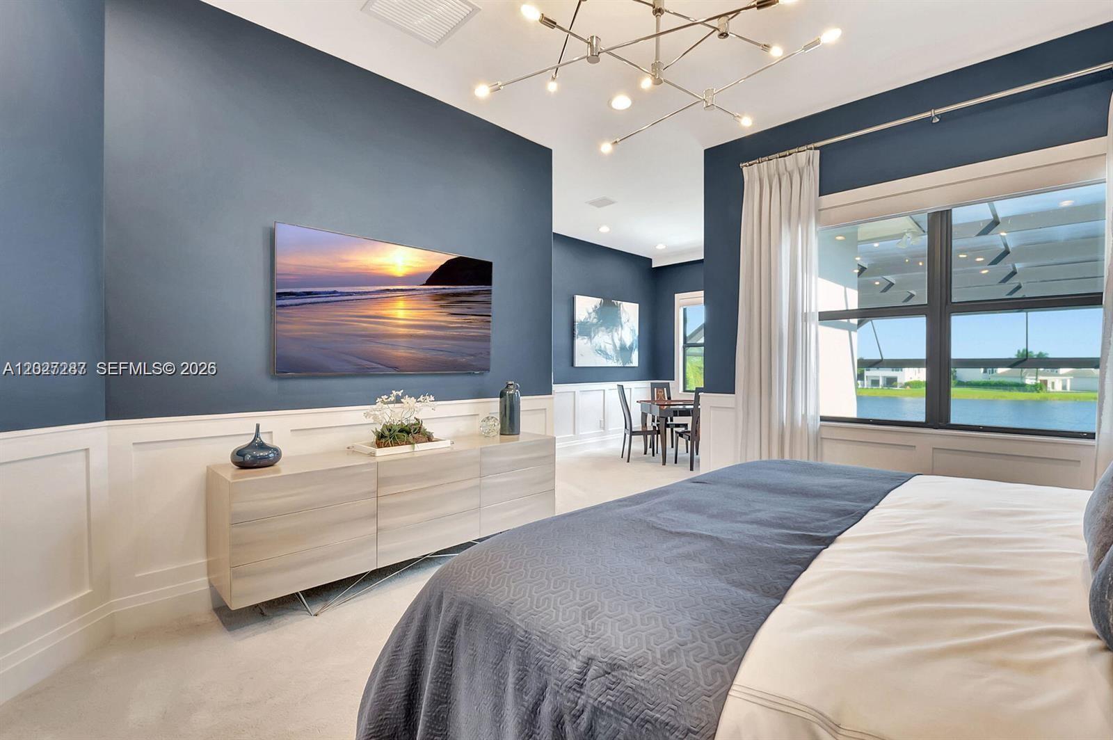 A bedroom features blue walls, white wainscoting, a modern chandelier, and a view of water — 17230 Brulee Breeze Way, Boca Raton FL 33496, BOCA RATON, FL