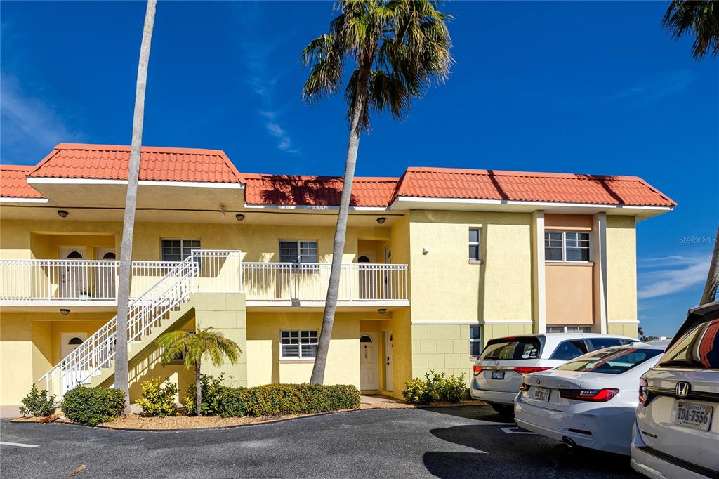 A two-story apartment building with yellow stucco walls, a red tile roof, and exterior stairs — 4103 GULF BOULEVARD UNIT 209, ST PETE BEACH, FL