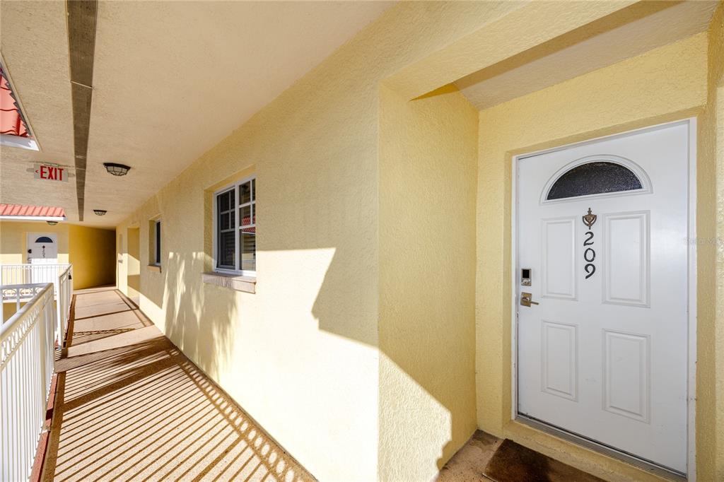 An exterior view of a yellow apartment building hallway with a white front door — 4103 GULF BOULEVARD UNIT 209, ST PETE BEACH, FL