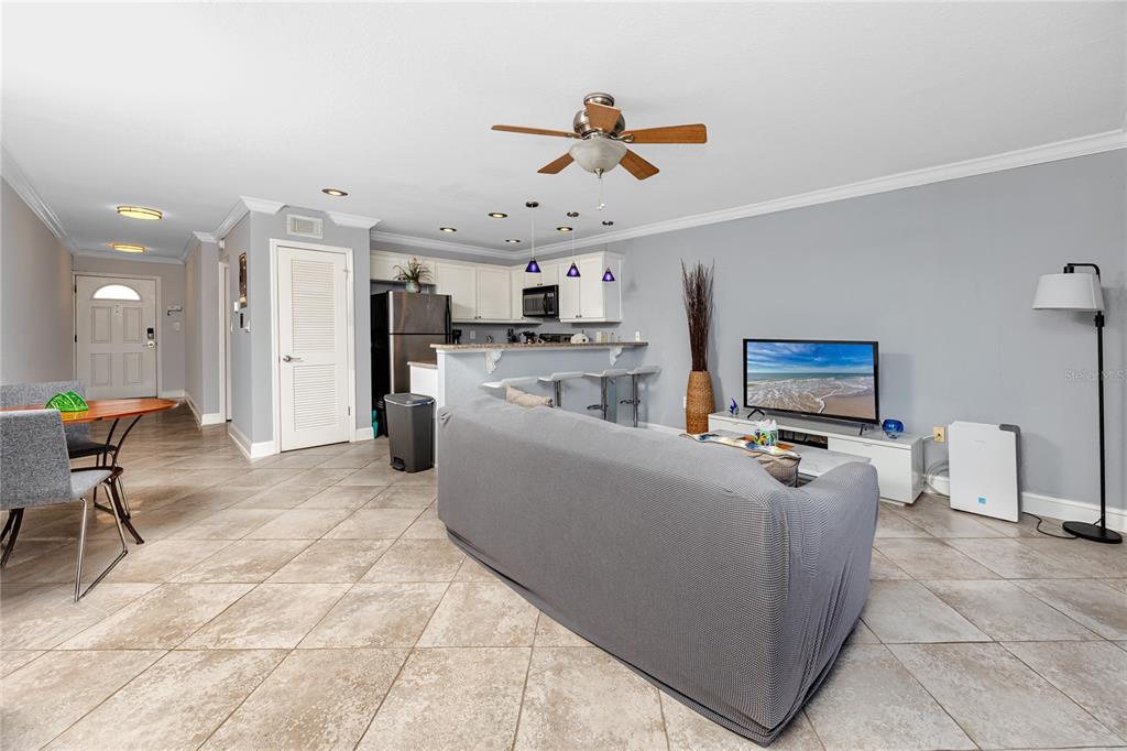 An open-concept living room and kitchen feature tile flooring, a gray sofa, and bar seating — 4103 GULF BOULEVARD UNIT 209, ST PETE BEACH, FL
