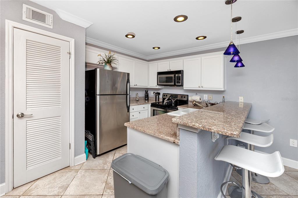 A kitchen features white cabinets, granite countertops, stainless steel appliances, and a breakfast bar — 4103 GULF BOULEVARD UNIT 209, ST PETE BEACH, FL