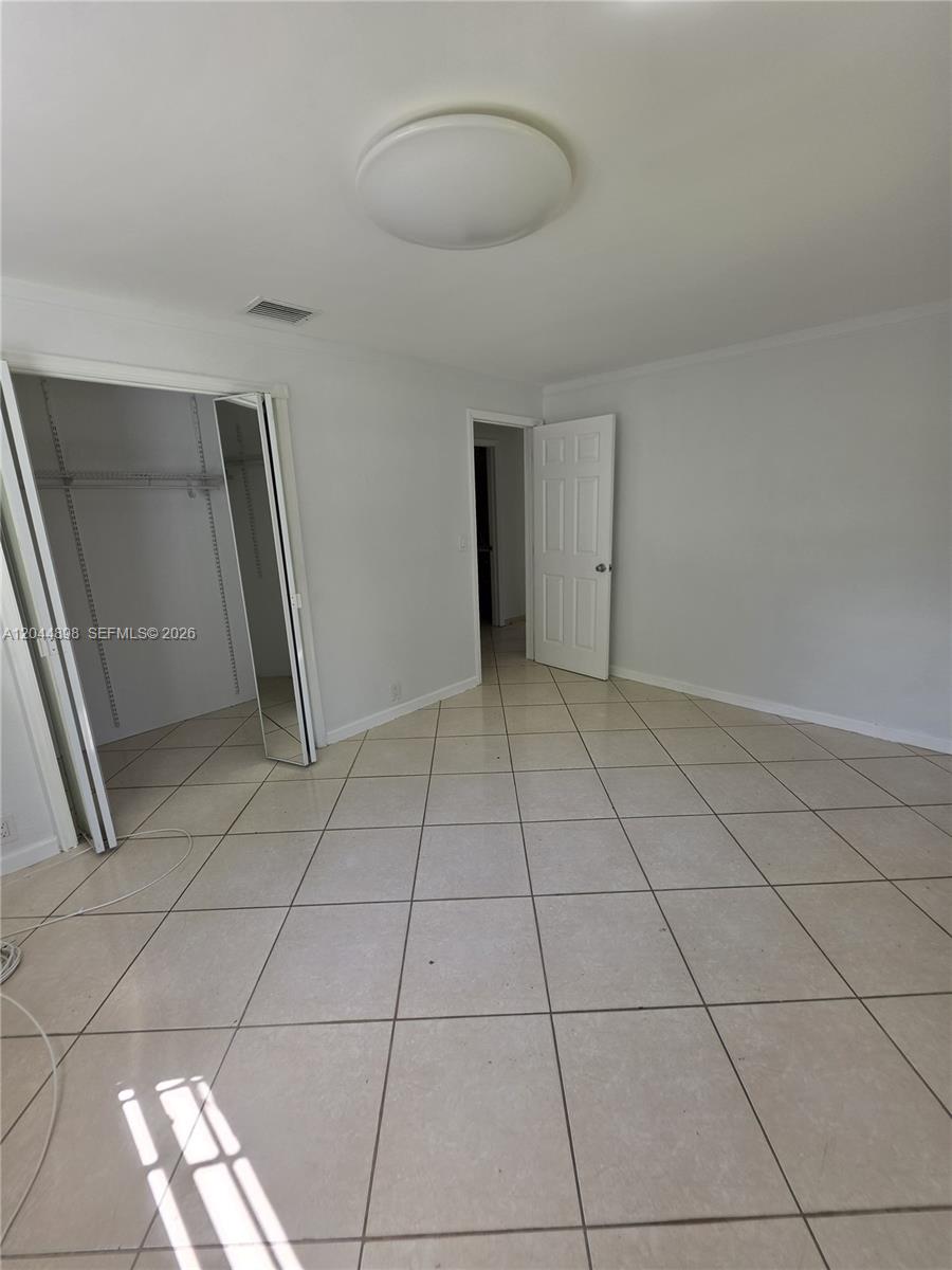 An empty room features light-colored floor tiles, white walls, a closet with mirrored doors, and a ceiling light — 5720 Douglas St, Hollywood FL 33021, HOLLYWOOD, FL