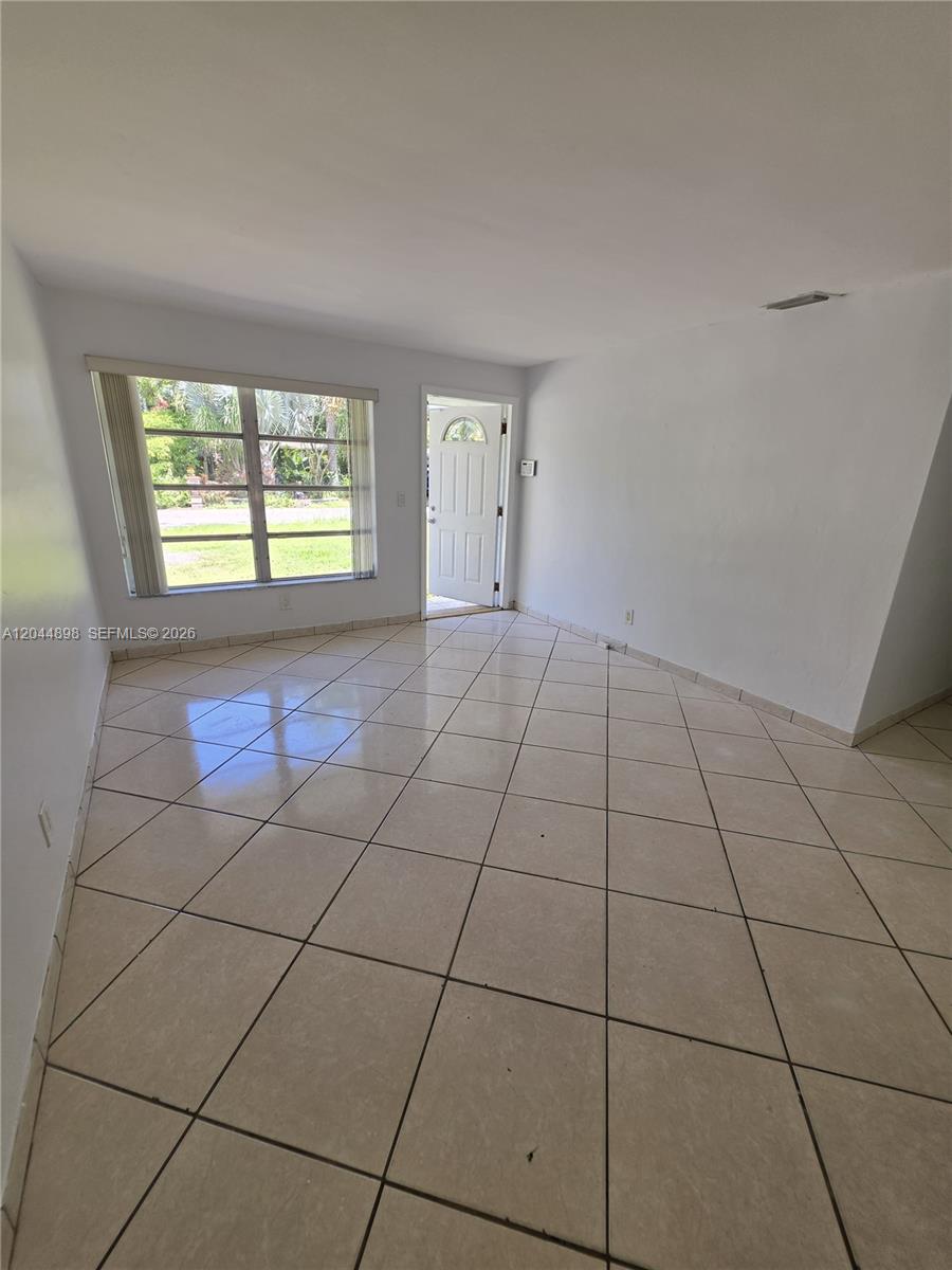 An empty room features white walls, a large window, and light-colored diagonal floor tiles — 5720 Douglas St, Hollywood FL 33021, HOLLYWOOD, FL