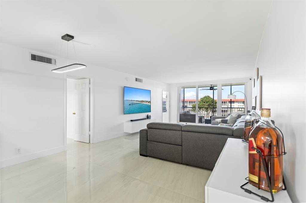 A modern living room features white tile floors, a gray sectional sofa, and a wall-mounted television — 3100 NE 48th Court # 413, Lighthouse Point FL 33064, LIGHTHOUSE POINT, FL