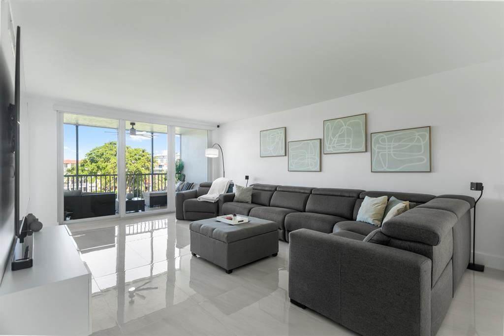 A modern living room features a large grey sectional, an ottoman, and sliding glass balcony doors — 3100 NE 48th Court # 413, Lighthouse Point FL 33064, LIGHTHOUSE POINT, FL