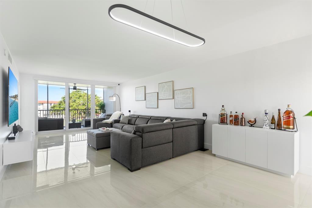 A modern living room features a grey sectional sofa, white cabinetry, and a large balcony — 3100 NE 48th Court # 413, Lighthouse Point FL 33064, LIGHTHOUSE POINT, FL