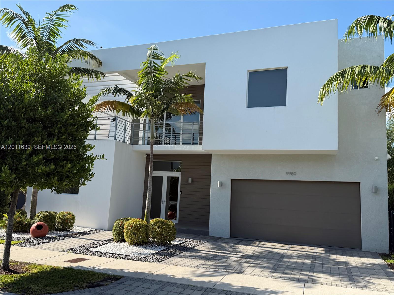 A modern two-story house features a white facade, a brown garage door, and palm trees — 9980 NW 74th Ter, Doral FL 33178, DORAL, FL