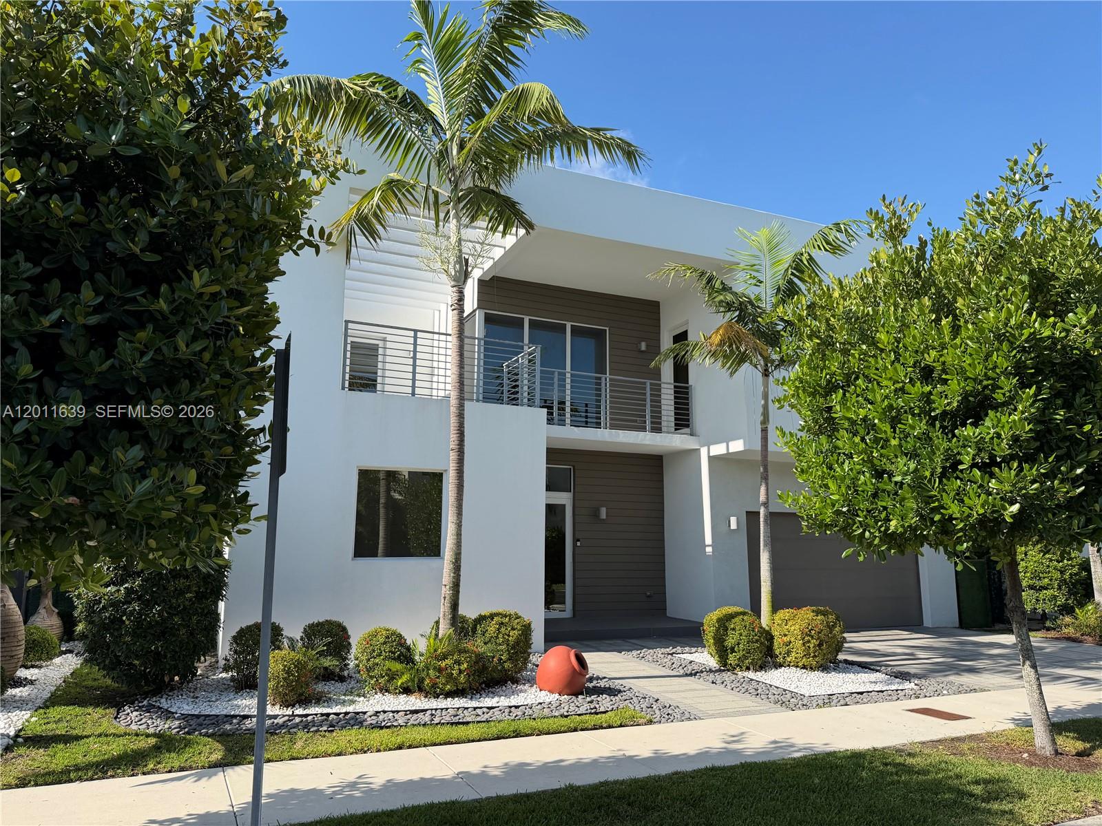 A modern two-story house features white stucco walls, wood-paneled accents, and a second-floor balcony — 9980 NW 74th Ter, Doral FL 33178, DORAL, FL