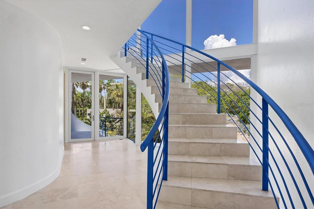 A curved staircase with blue railings stands in a bright foyer with light tile floors — 5801 GULF OF MEXICO DRIVE, LONGBOAT KEY, FL