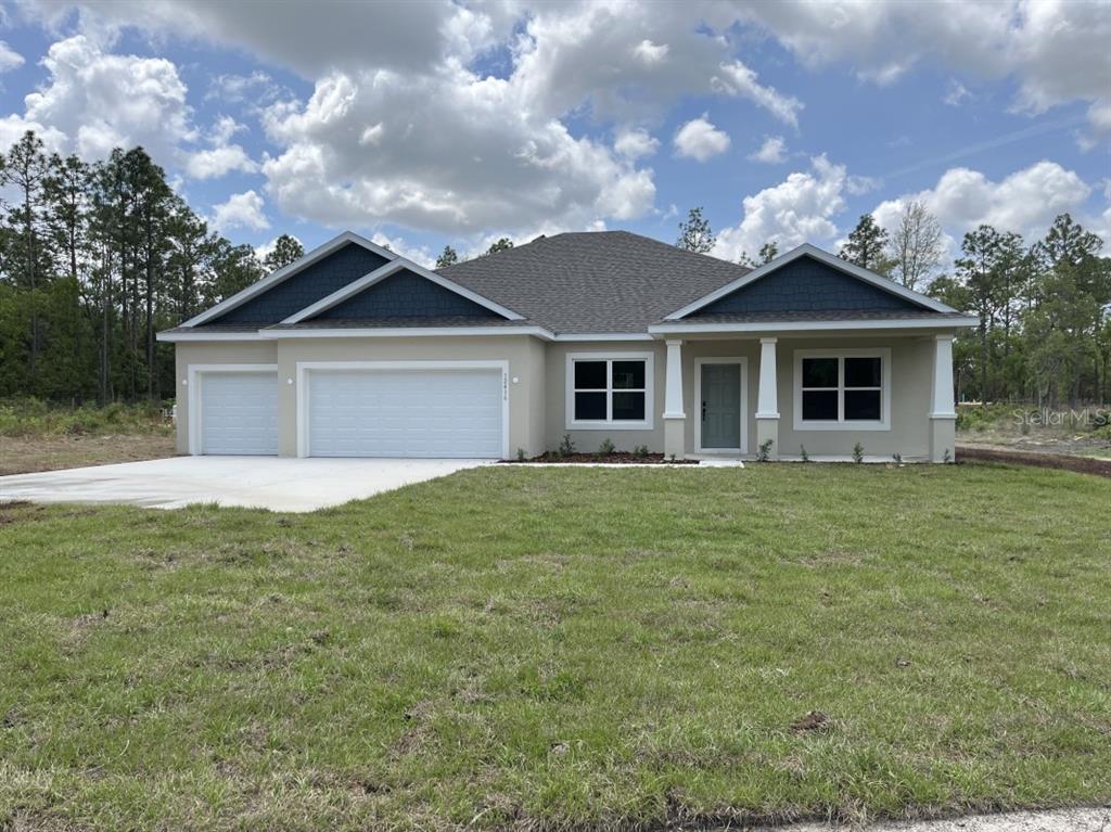 A single-story house with a three-car garage, tan stucco siding, and blue gable accents — 12416 SW 67TH LANE, OCALA, FL