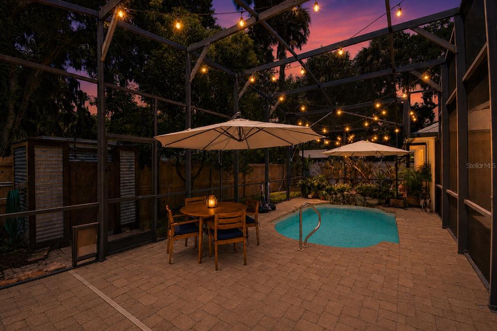 A screened-in patio features a small swimming pool, dining set, and overhead string lighting — 1112 PALMETTO STREET, NEW SMYRNA BEACH, FL