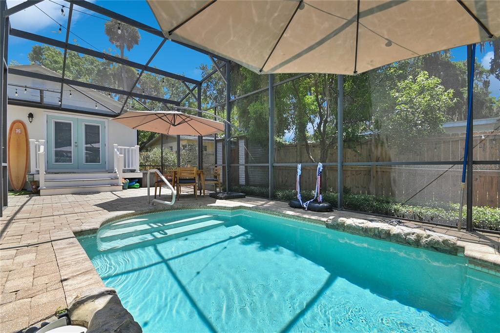 A screened-in patio features a swimming pool, a patio table, and a surfboard — 1112 PALMETTO STREET, NEW SMYRNA BEACH, FL