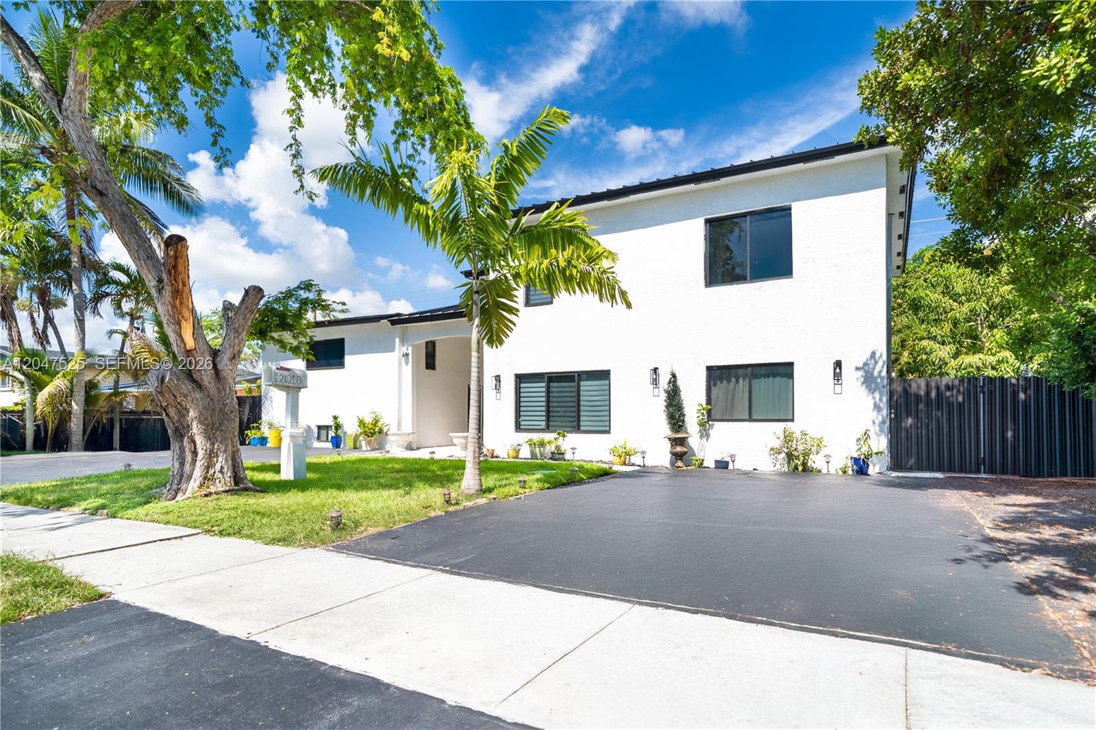 A two-story white house with black window frames and a paved driveway under a blue sky — 20200 NE 14th Ave, Miami FL 33179, MIAMI, FL