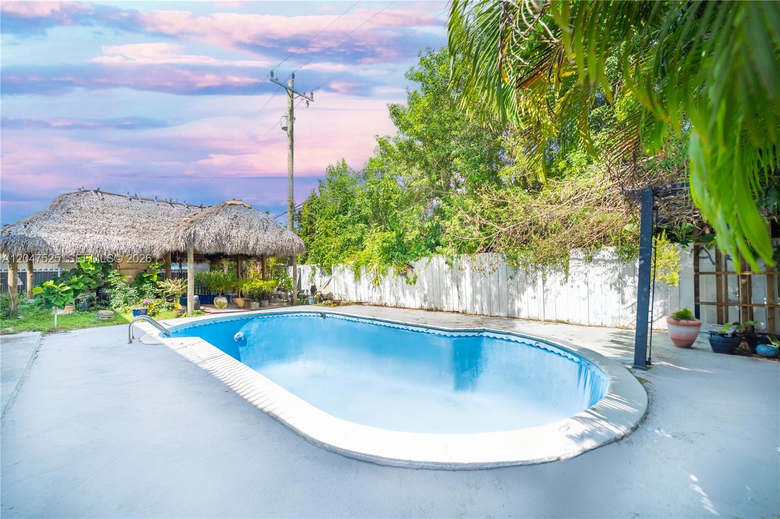 An outdoor swimming pool sits on a concrete patio next to a thatched-roof tiki hut — 20200 NE 14th Ave, Miami FL 33179, MIAMI, FL