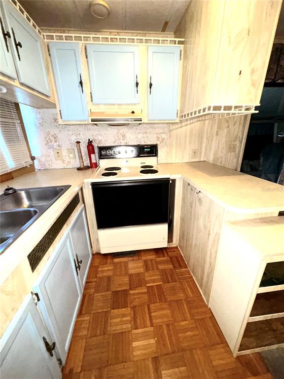 A kitchen features light blue cabinets, a white stove, and wood parquet flooring — 22 WOODRUFF WAY, LAKE WALES, FL